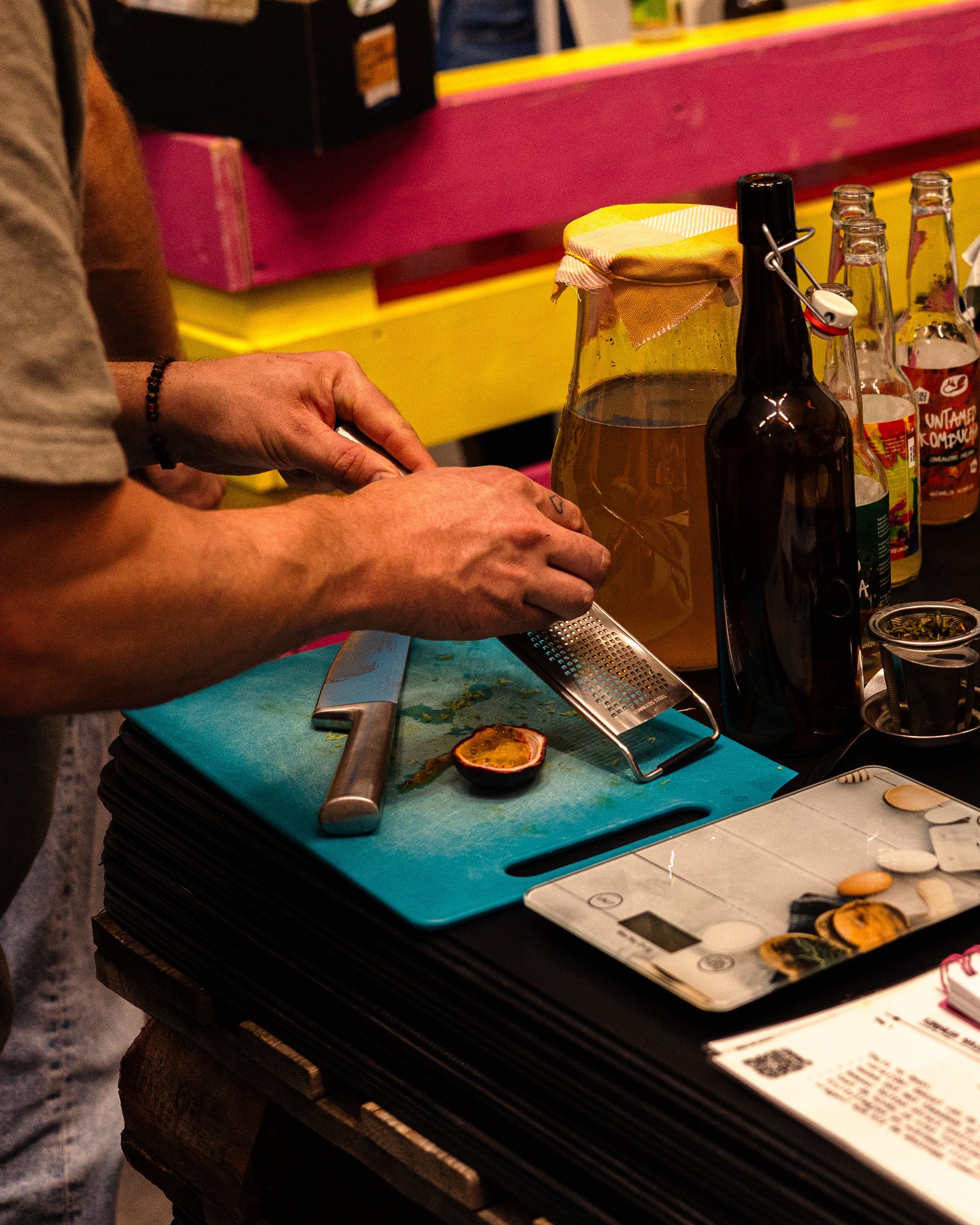Een snijplank met passievrucht en een workshopdeelnemer die limoen schaaft om te gebruiken in kombucha. Op de achtergrond een schaaltje met groene thee