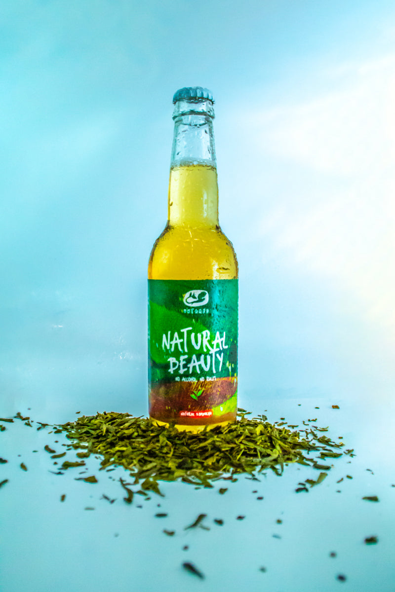 Een flesje Natural Beauty van Untamed Kombucha met theeblaadjes aan de voet