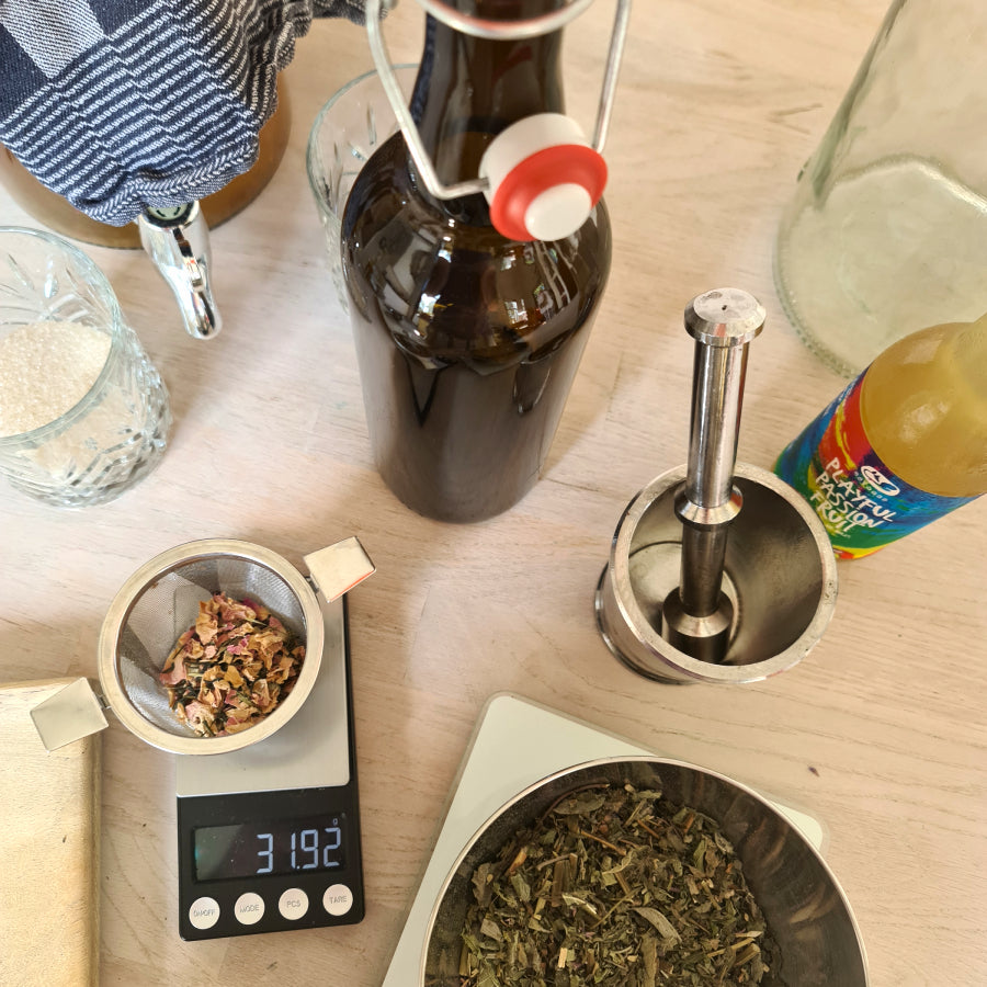 Een close up van een kombucha workshop, met een grote fles, weegschaal, thee en kombucha