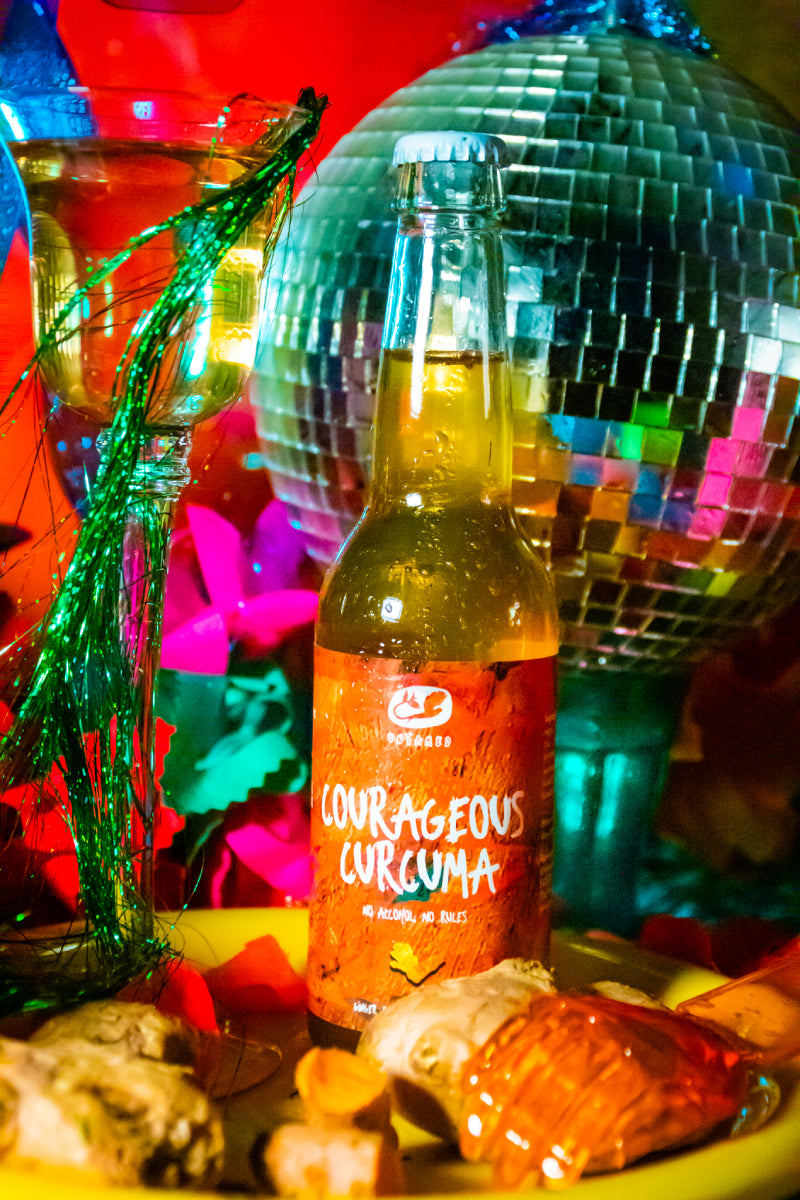 Een flesje courageous curcuma kombucha met een disco achtergrond.