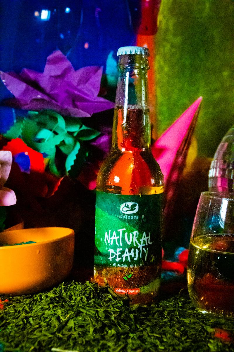 Een flesje Natural Beauty van Untamed Kombucha met een disco achtergrond